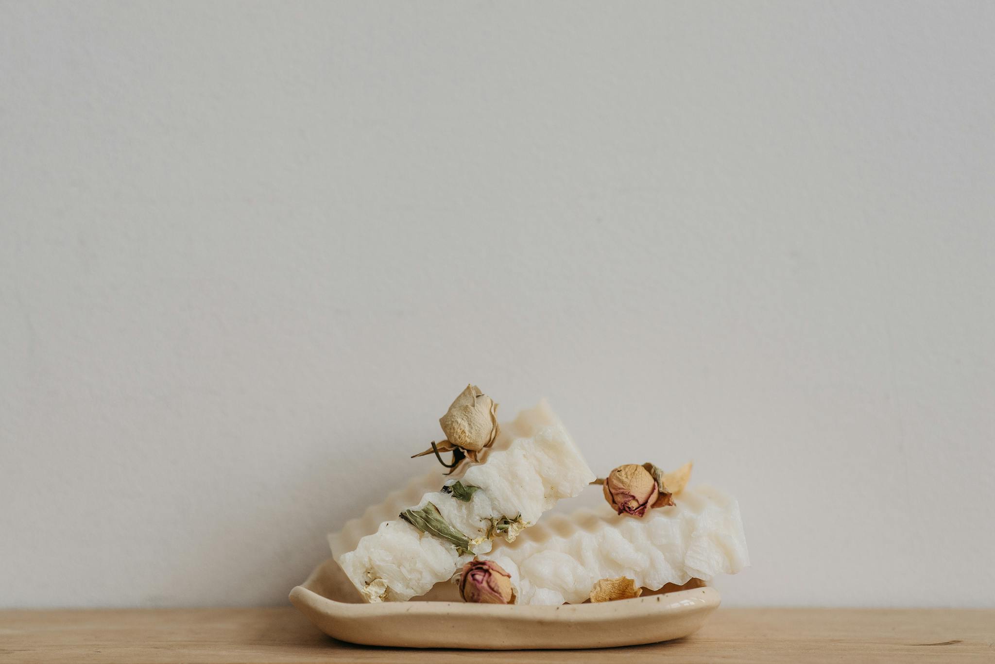 Eco-friendly white soap bars with dried flowers on a ceramic tray, perfect for sustainable living.
