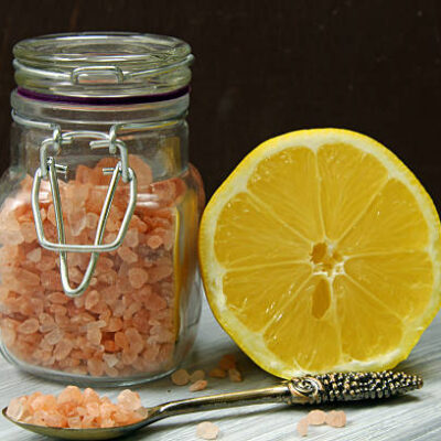A jar of himalayan salt and a lemon on a wooden baackground.