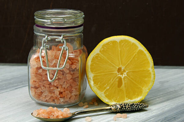 A jar of himalayan salt and a lemon on a wooden baackground.